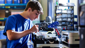 Man in blue tshort with tools working on a printer on a work bench