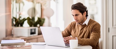 A man looking concerned reading an email on his notebook computer while sat at a table in a home working environment