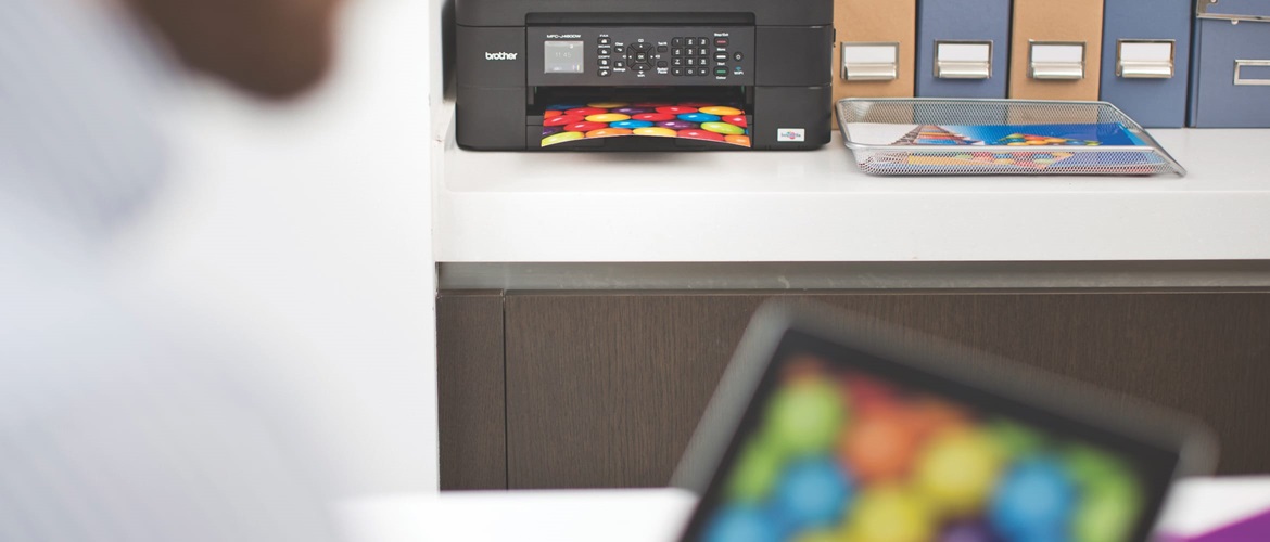 A person wirelessly printing a colourful image from an iPad to a Brother inkjet printer