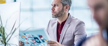 A businessman checking a printed image against the original digital version on a desktop computer