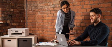 Male and female colleagues connecting a printer to a Wi-Fi network in a small office environment