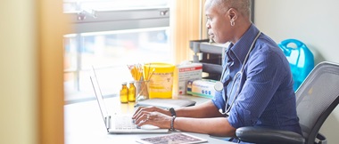 Female doctor typing on a notebook computer while sat at her desk in a surgery