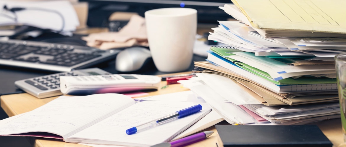 messy office work desk covered in files, cups, papers and pens