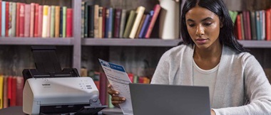 Lady sat at a desk using a laptop and scanning a document on a Brother scanner