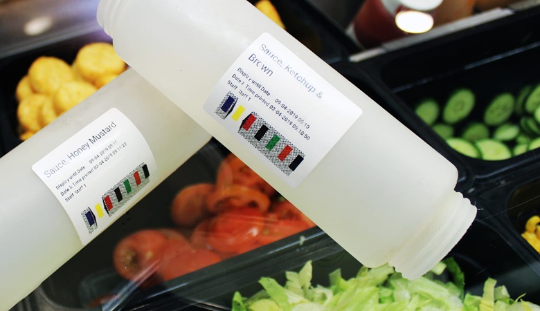 Two empty sauce containers, one labelled Honey Mustard and the other Ketchup and Brown, with salad trays in the background