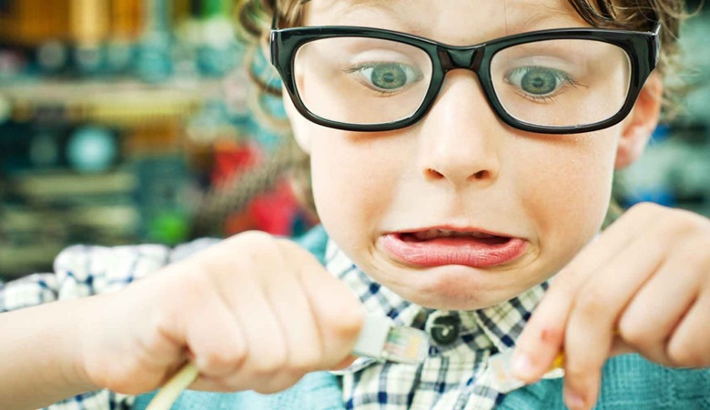 Young boy wearing glasses pulling a face while holding two ends of a computer cable