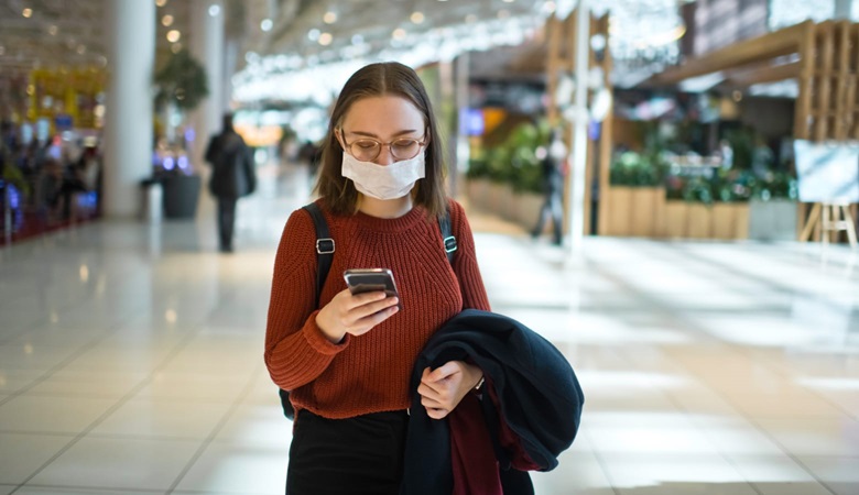 Young woman checking her smartphone while wearing a face mask in an indoor retail shopping centre