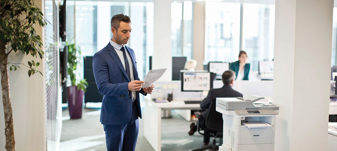 Man checking a piece of paper whilst standing next to a printer in an office