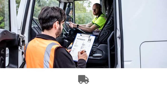 Man sat in truck, door open, man in orange hi-vis stood holding clipboard