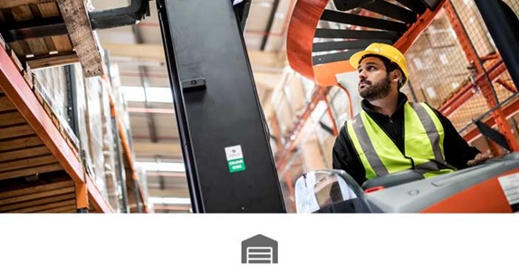 Male warehouse operativewearing yellow hard hat and hi-vis in forklift moving pallet